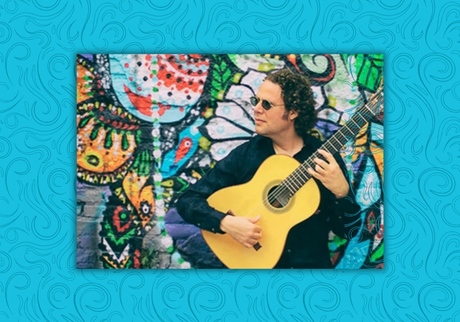 Mr. del Monte holding a guitar in front of a brightly painted wall