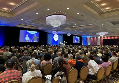 Chris and Alisa speaking in front of a large crowd at a conference