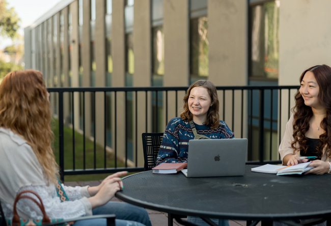 Three students talking and using laptops outside