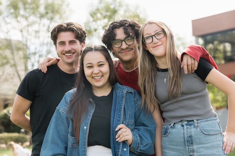Group of four students smiling together outside