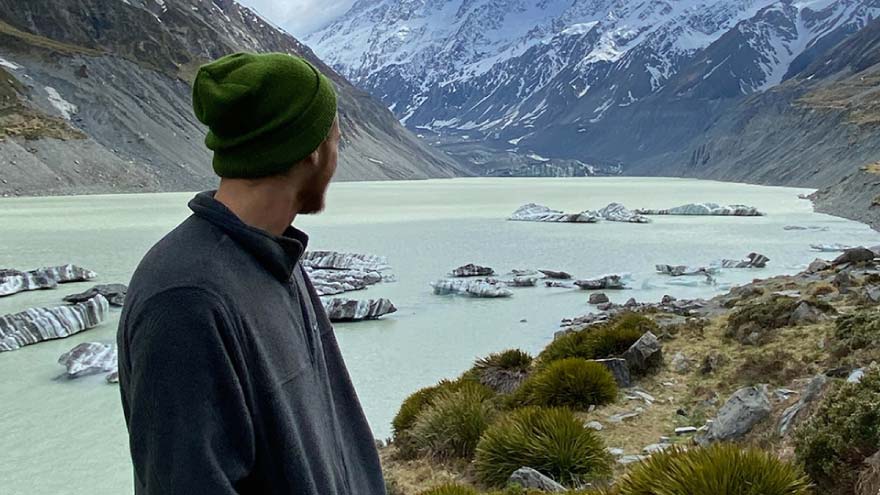 a young man looking at a lake with mountains in the background