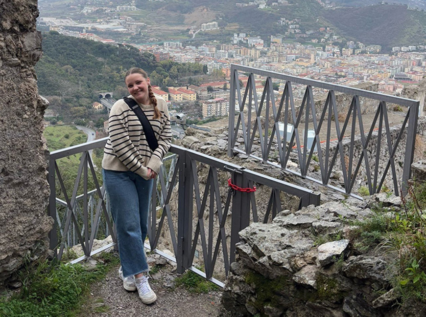 student posing in front of village